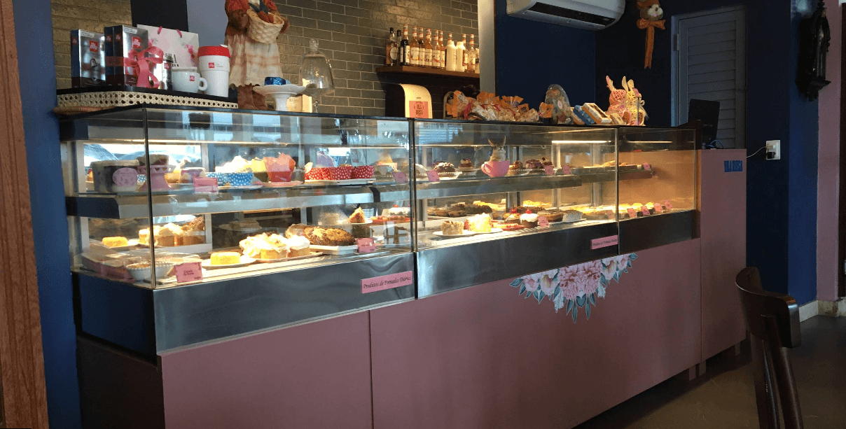 Balcão rosa da Vila Rosa Café com a vitrine iluminada cheia de bolos, tortas e doces