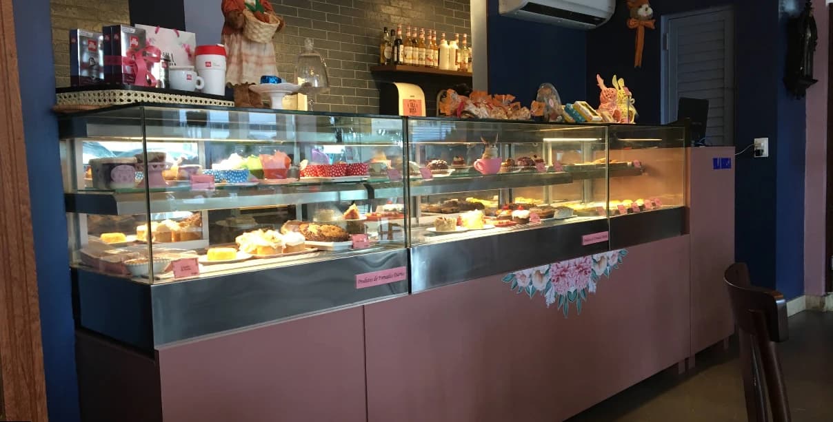 Balcão rosa da Vila Rosa Café com a vitrine iluminada cheia de bolos, tortas e doces